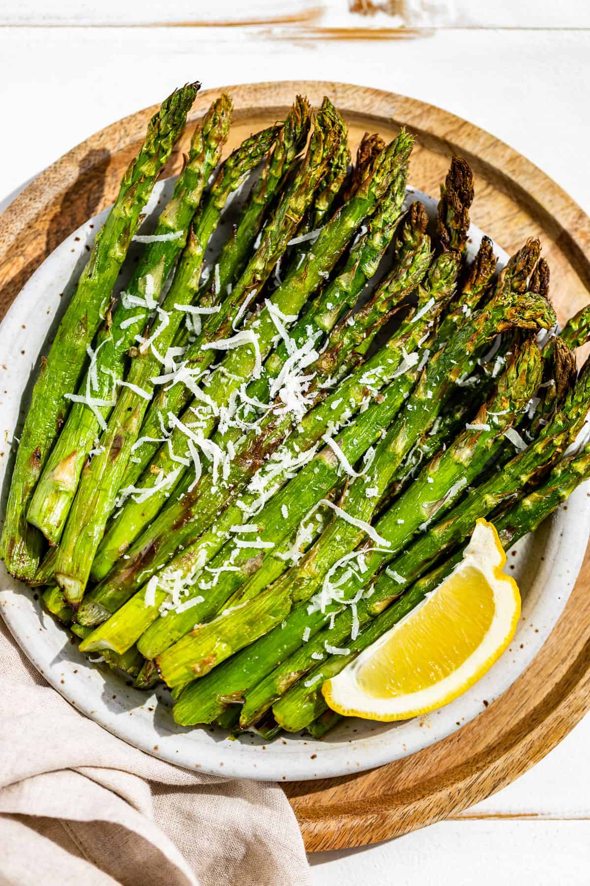 Air fryer asparagus on a pottery plate placed on a round wooden plate with a lemon wedge on the side.