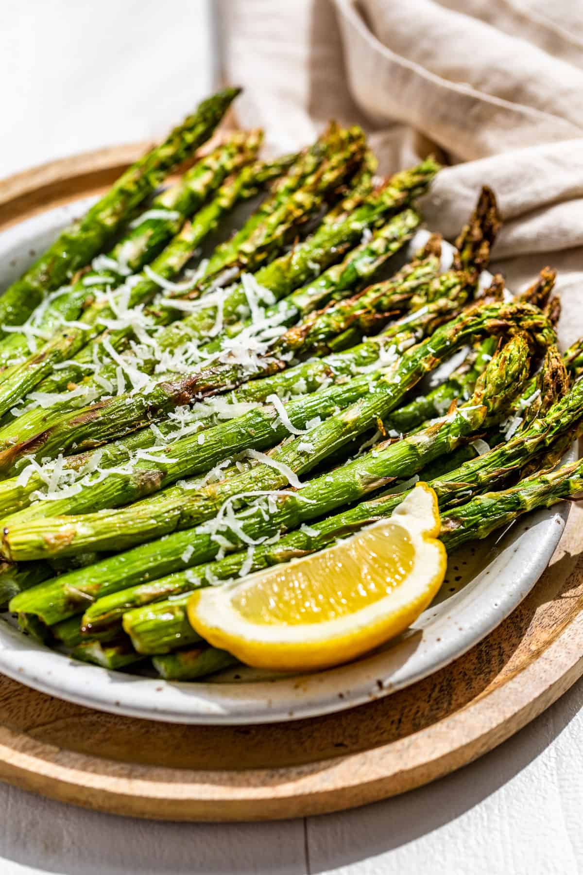Side view of Air fryer asparagus on a pottery plate sprinkled with parmesan and a lemon wedge on the side.