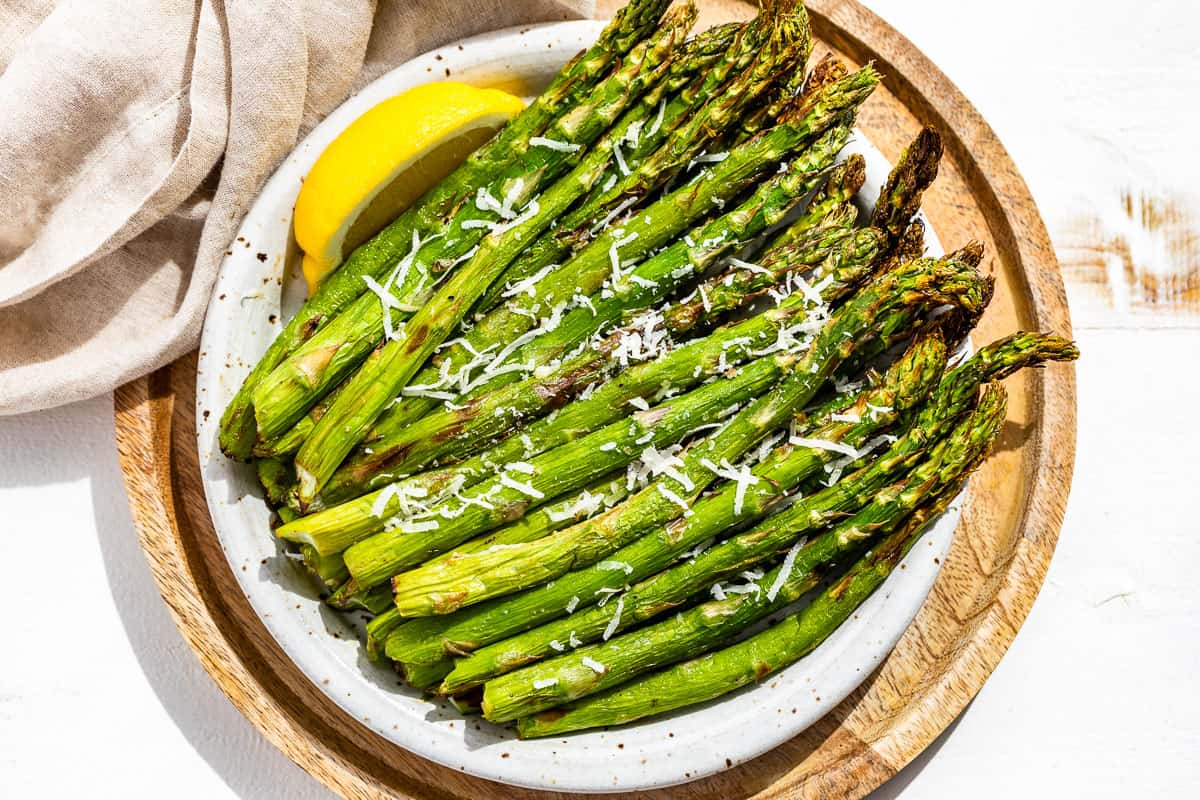 Finished air fryer asparagus on a pottery plate with a lemon wedge on the side sitting on a round wood plate.