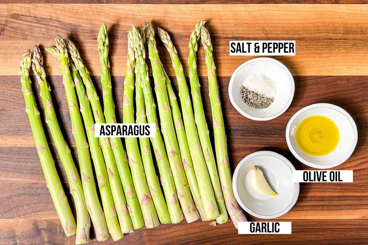 Fresh asparagus, olive oil, garlic, salt and pepper on a wood cutting board.