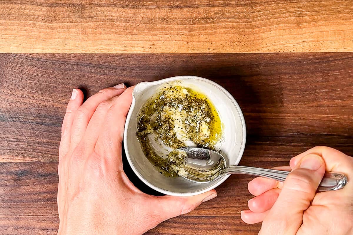 Mixing together the garlic, sea salt, pepper, and olive oil in a small pottery bowl.