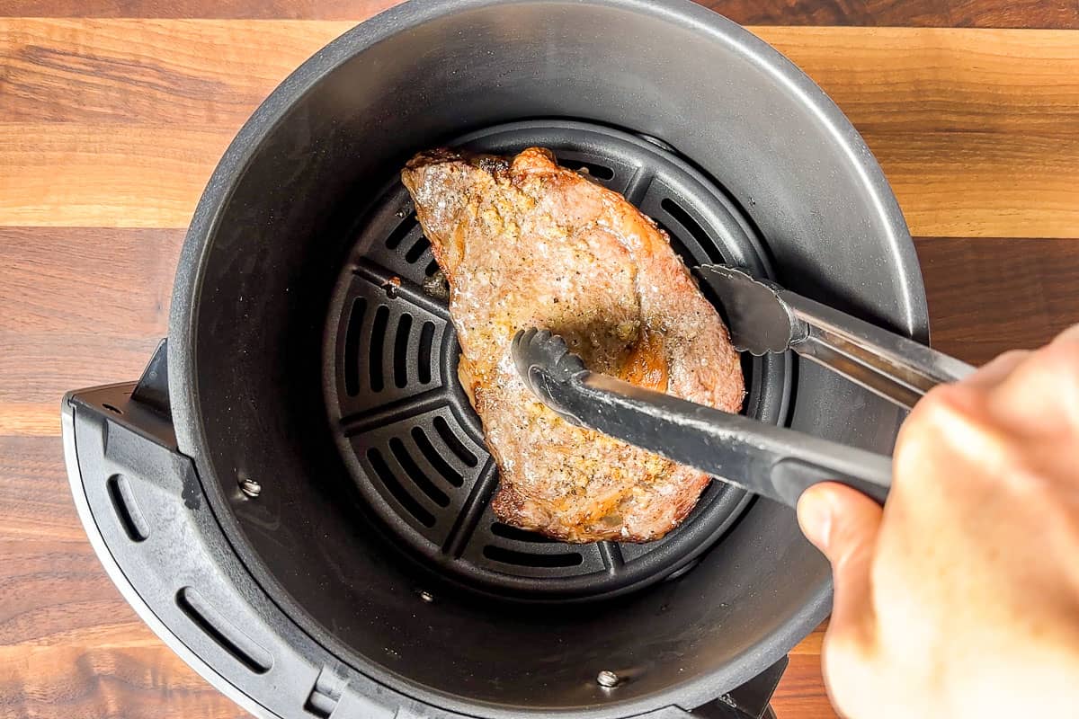 Turning the ribeye steak halfway through the cooking time.