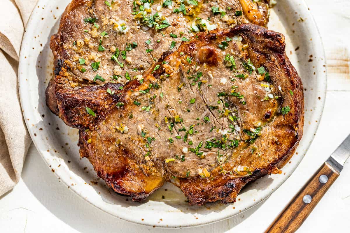 Browned air fryer ribeye steaks on a pottery plate drizzled with garlic butter and sprinkled with parsley.