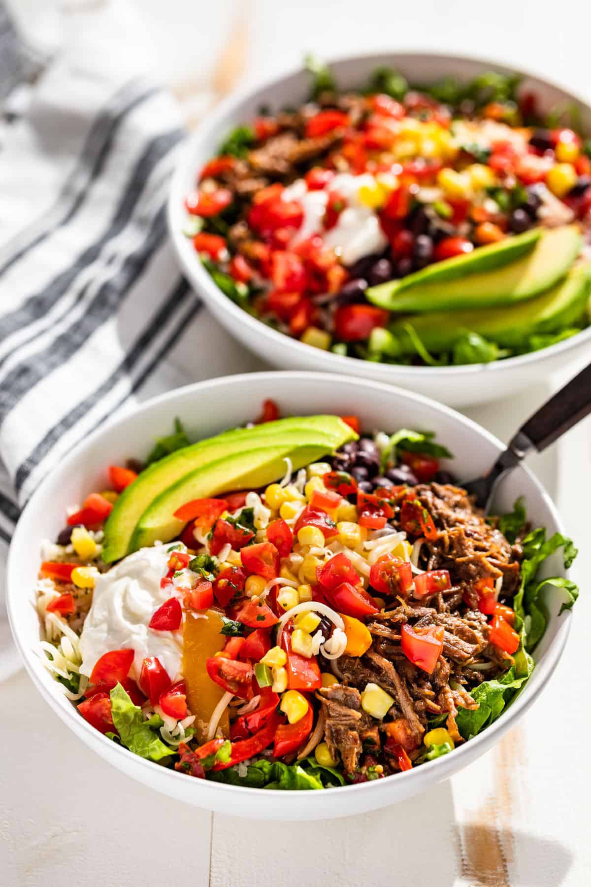 Side view of two Beef Barbacoa Burrito Bowls with forks in the side of the bowls on a white background.