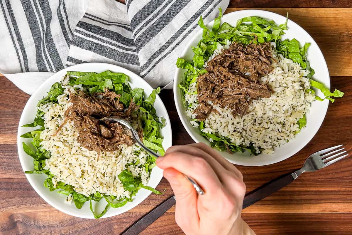 Topping the lettuce and cilantro lime rice with shredded Beef Barbacoa in two white bowls.