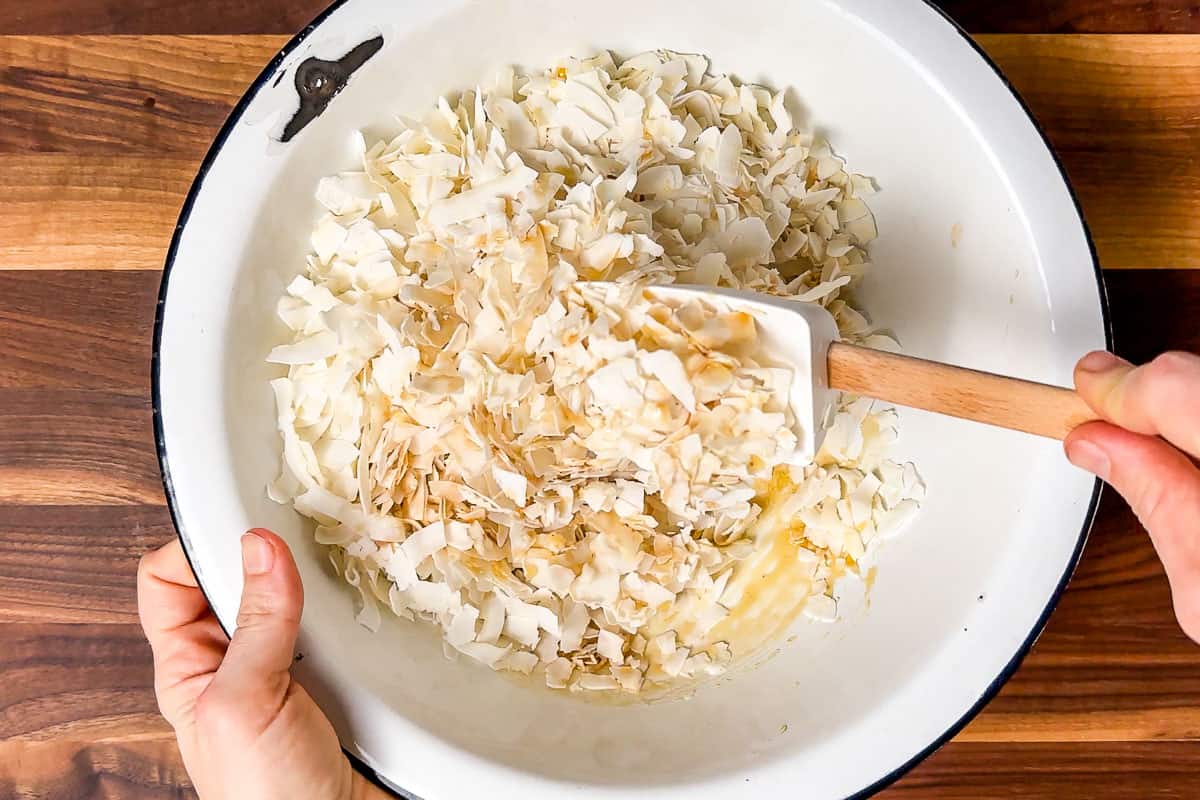 Mixing together the maple syrup, vanilla and coconut flakes together in a large white bowl.
