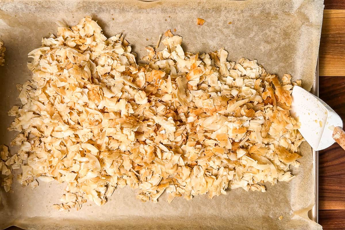 Stirring the light golden brown coconut chips halfway through the baking time.