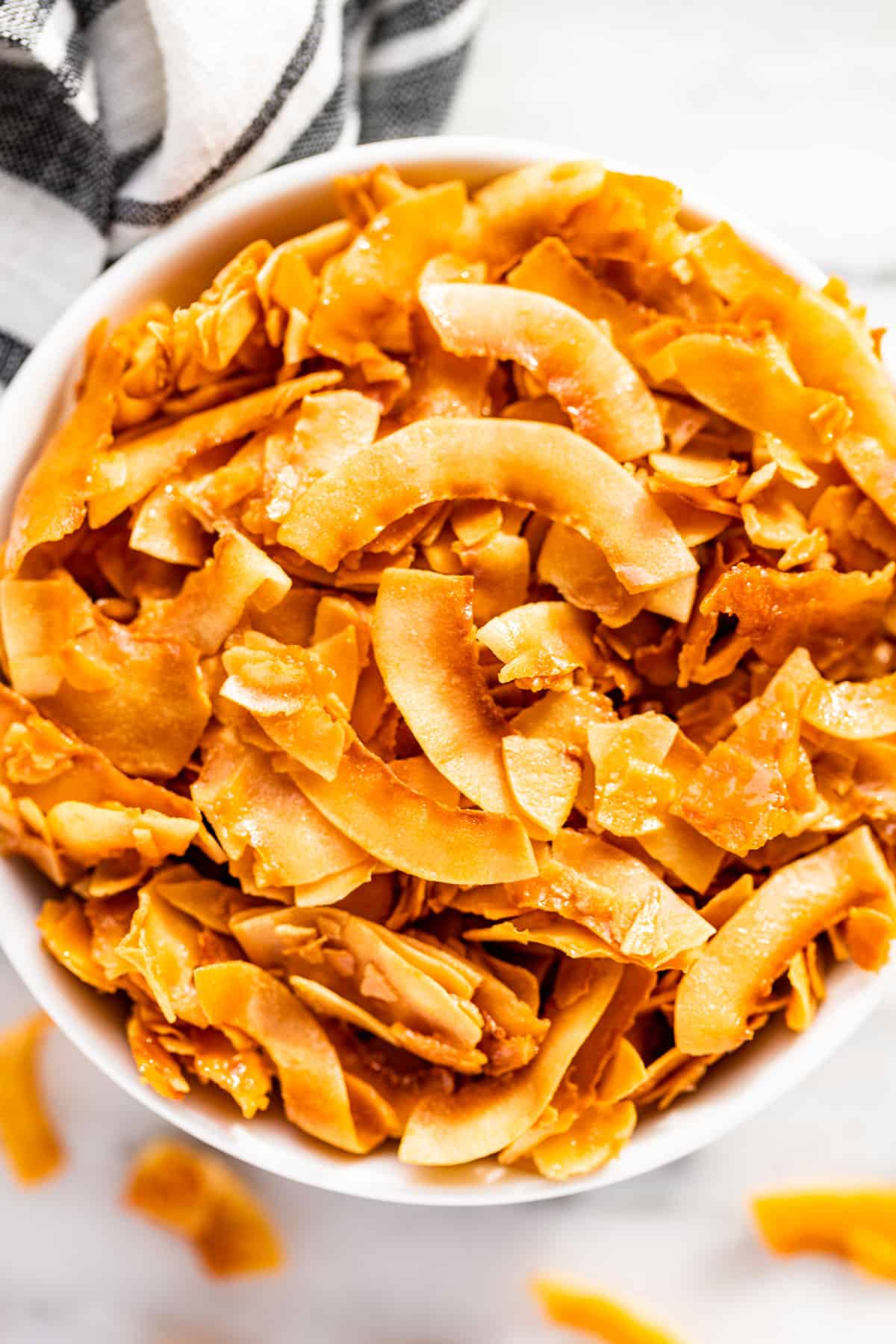 Close up view of Coconut Chips in a white bowl with a blue and white linen in the background.