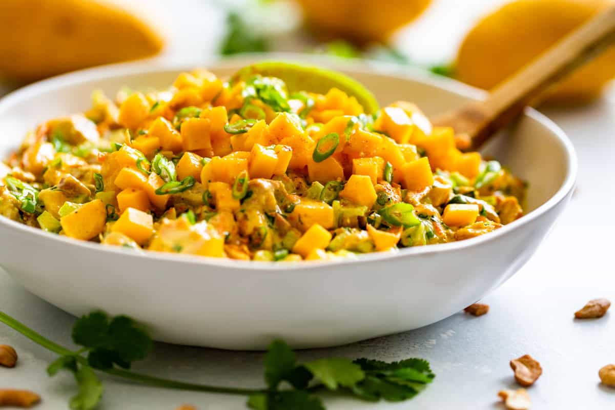 Side view of the finished Curried Chicken Salad in a white bowl topped with diced mango and a lime wedge.