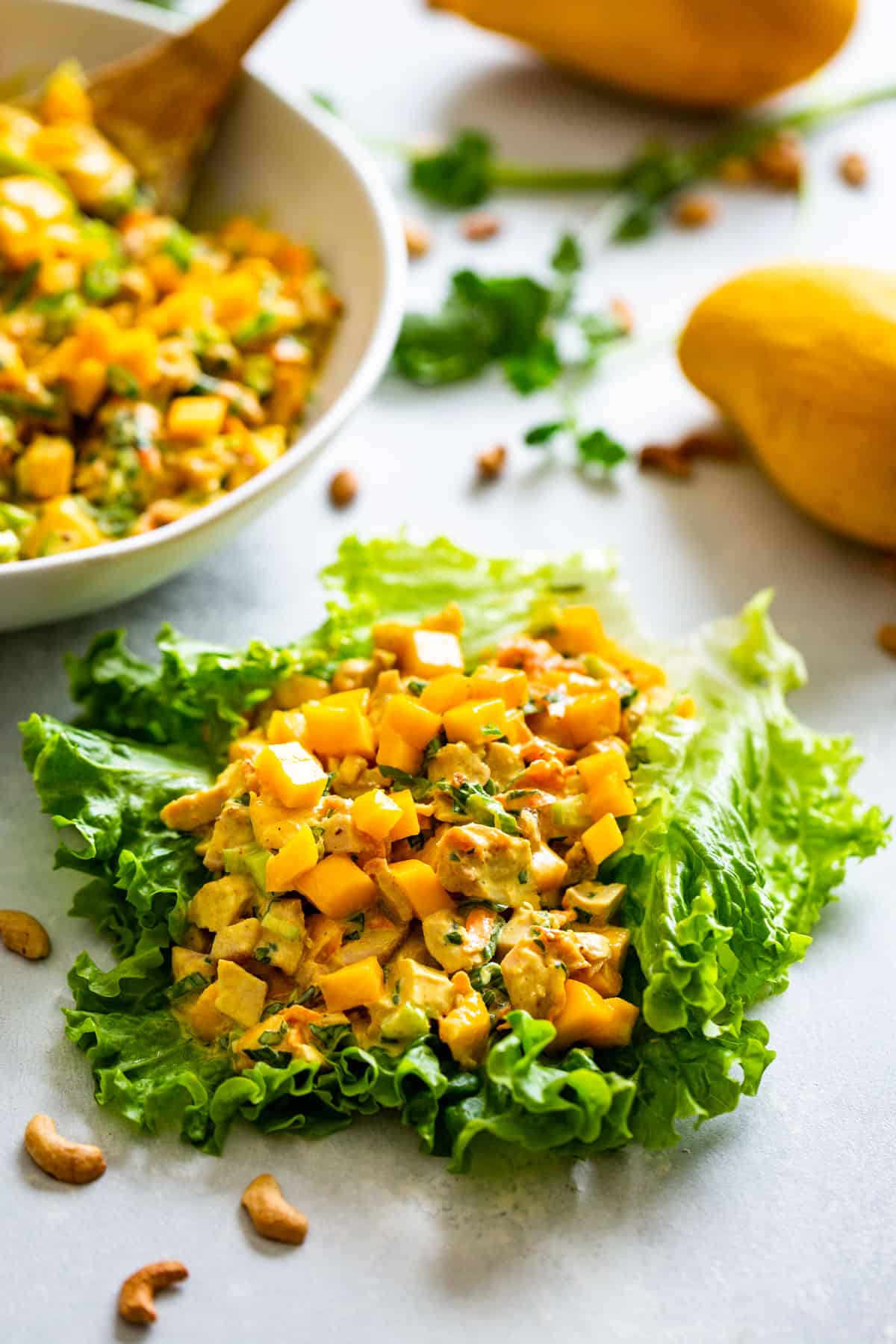 Curried Chicken Salad on a large lettuce leaf with a bowl of chicken salad and mangoes in the background.