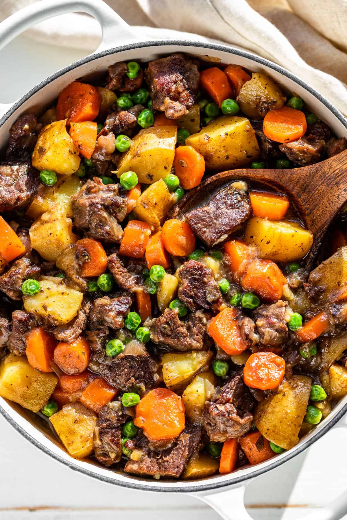 Straight down view of Beef Stew in a white Dutch oven with a wood ladle in it.