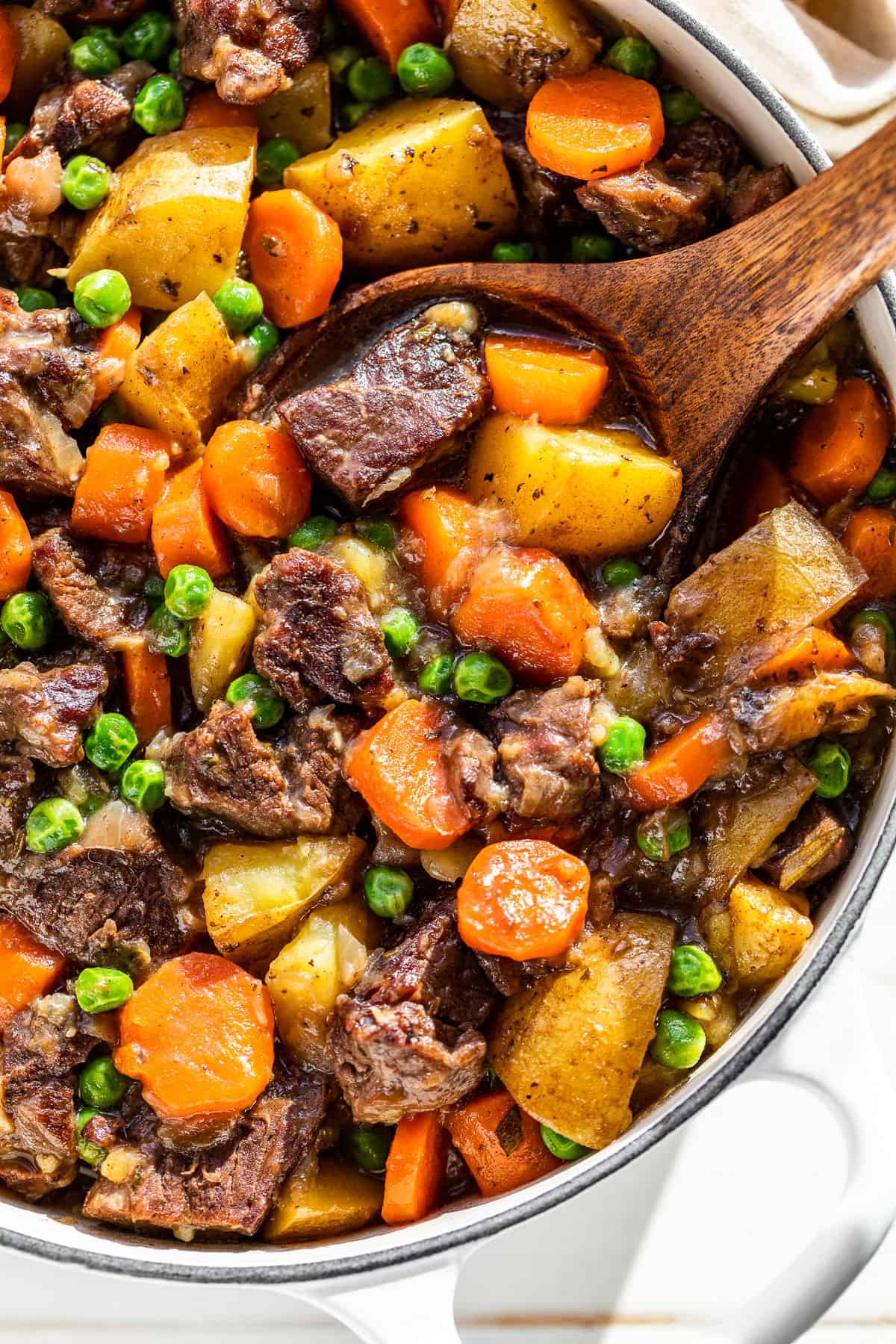 Close up downwards view of Dutch Oven Beef Stew in a white Dutch Oven with a wood ladle scooping some out.