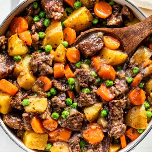 Finished Beef Stew in a white Dutch oven with a wood ladle in it.