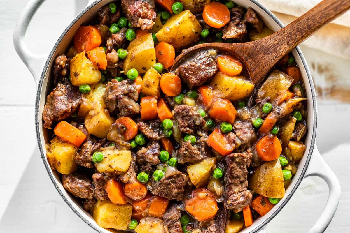 Finished Beef Stew in a white Dutch oven with a wood ladle in it.