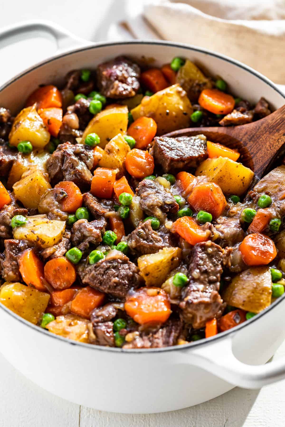 Side view of Dutch Oven Beef Stew in a white Dutch oven pot with a wood ladle in it.