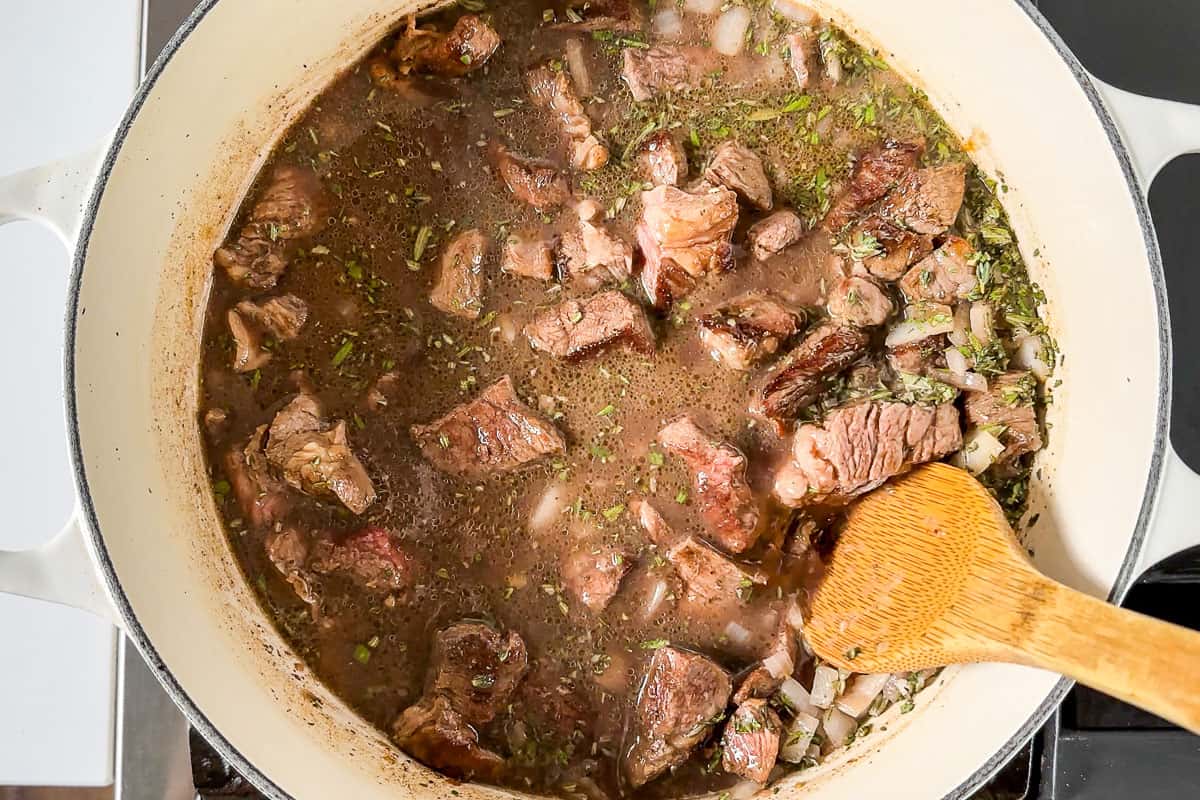 Adding the browned stew meat to the cooked onions with the beef broth.