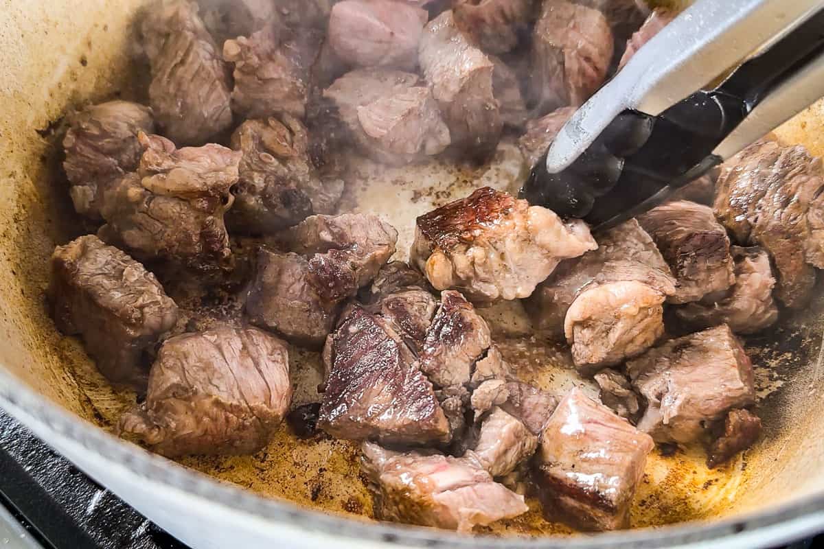 Browning the stew meat in a white Dutch oven pot.