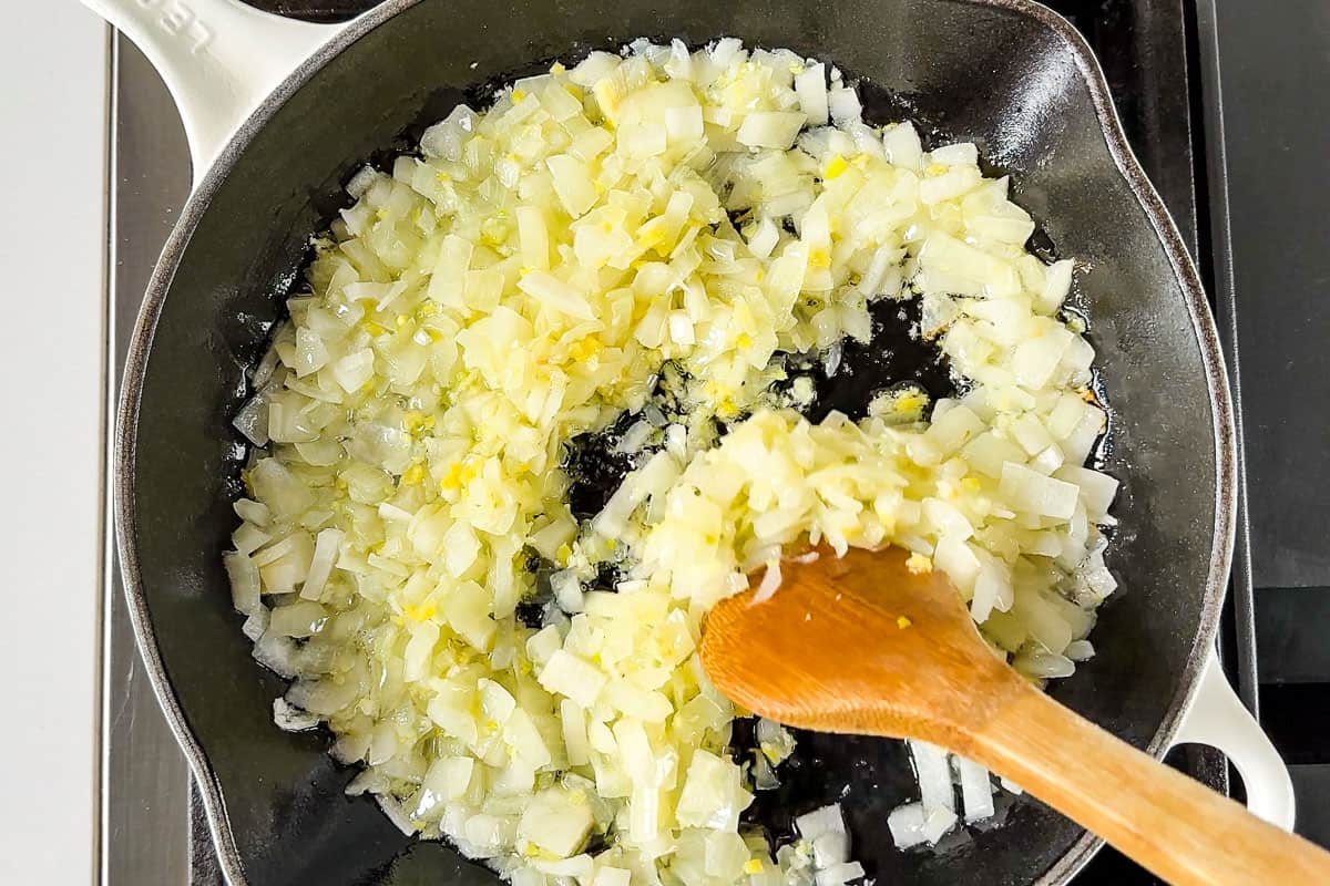Sautéing the onion, garlic, and ginger together in a white cast iron skillet.