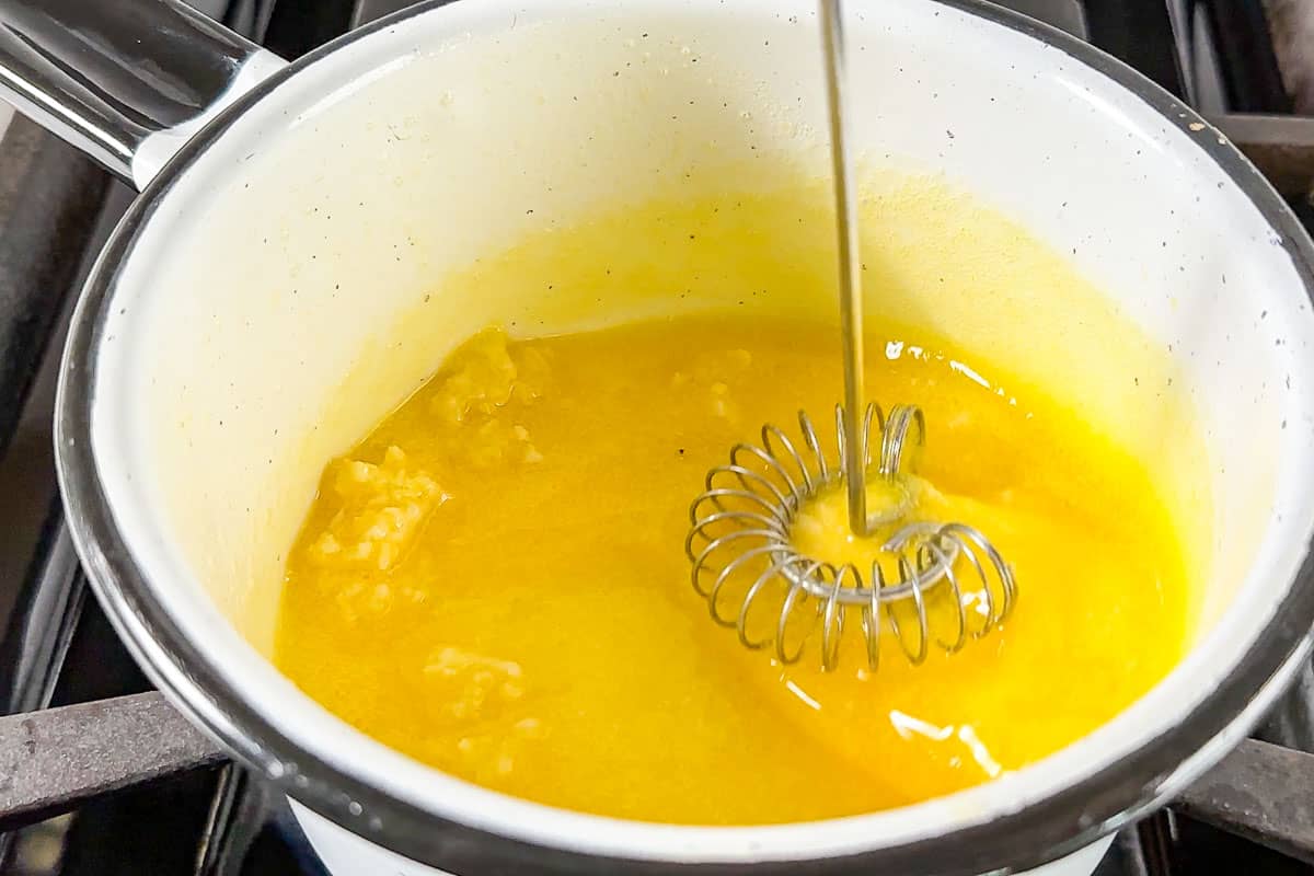 Whisking the minced garlic into the melted butter in a small white saucepan.