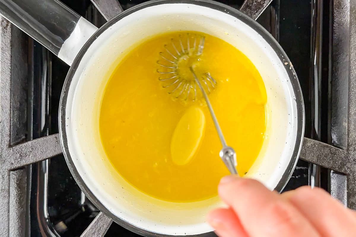 Melting the butter in a small white saucepan on a gas cooktop.
