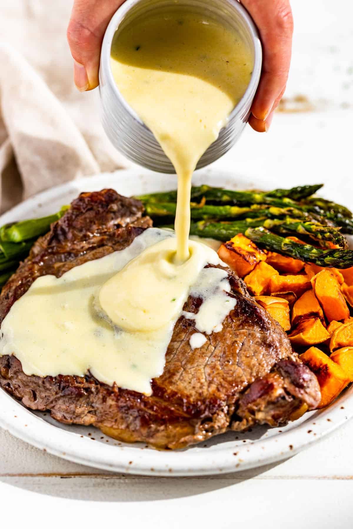 Drizzling the garlic parmesan cream sauce over a steak with roasted cubed sweet potatoes and asparagus on the side.