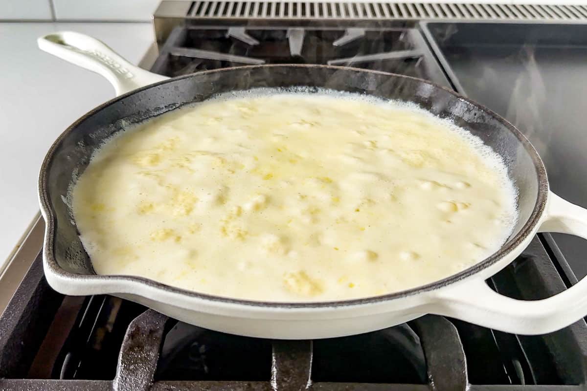 Simmering the garlic cream mixture in a white enameled skillet.