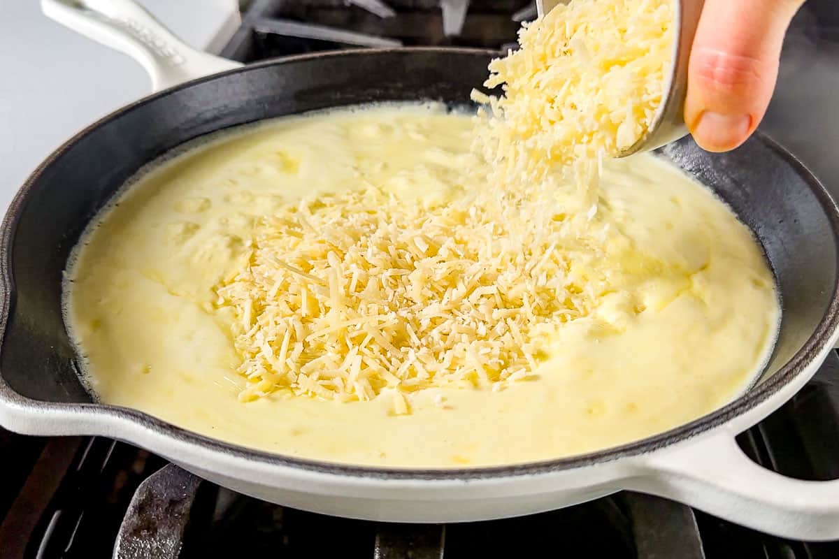 Adding grated parmesan cheese to the simmering garlic cream sauce.
