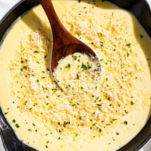 Finished Garlic Parmesan Sauce topped with grated parmesan and chopped parsley in a white enameled skillet with a wood spoon in it.