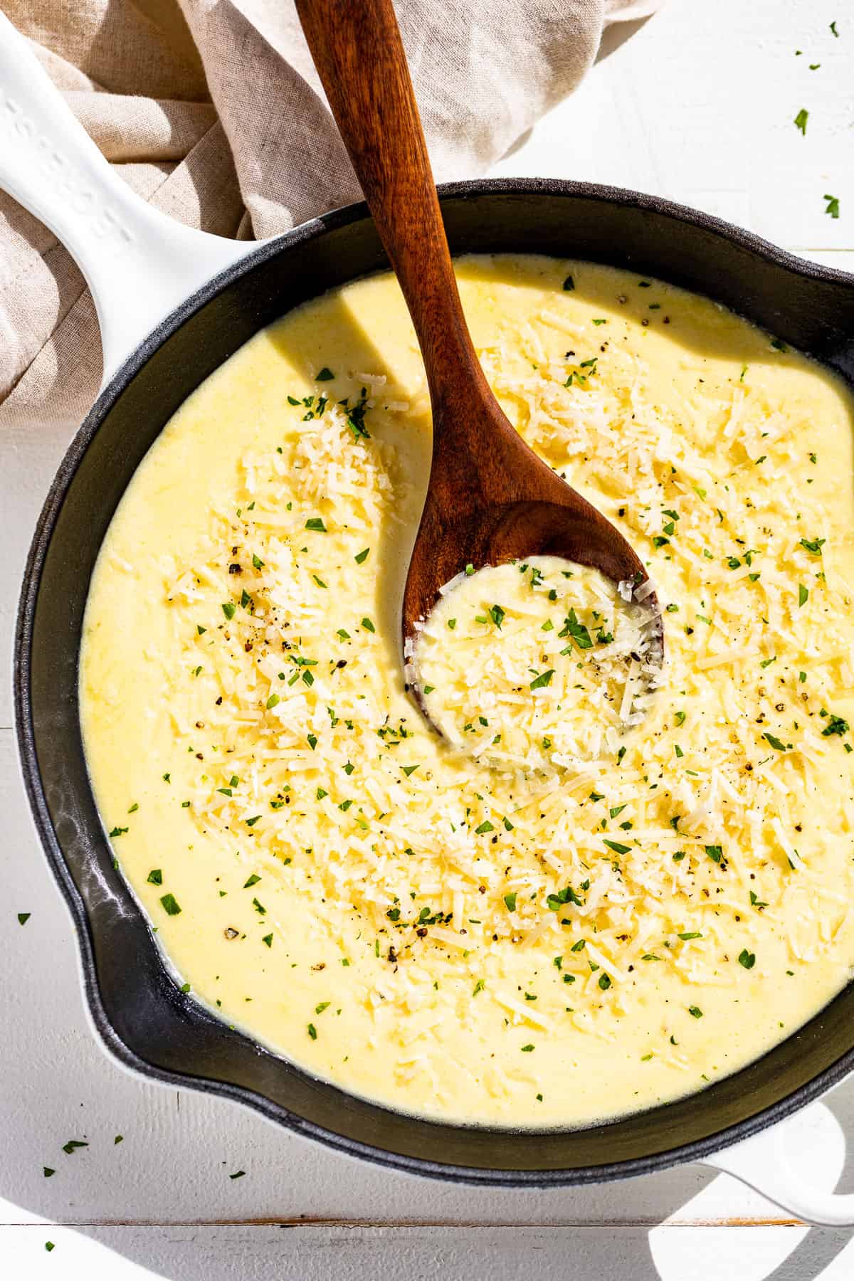 Straight down view of creamy Garlic Parmesan Sauce in a white enameled skillet with a wood spoon in it.