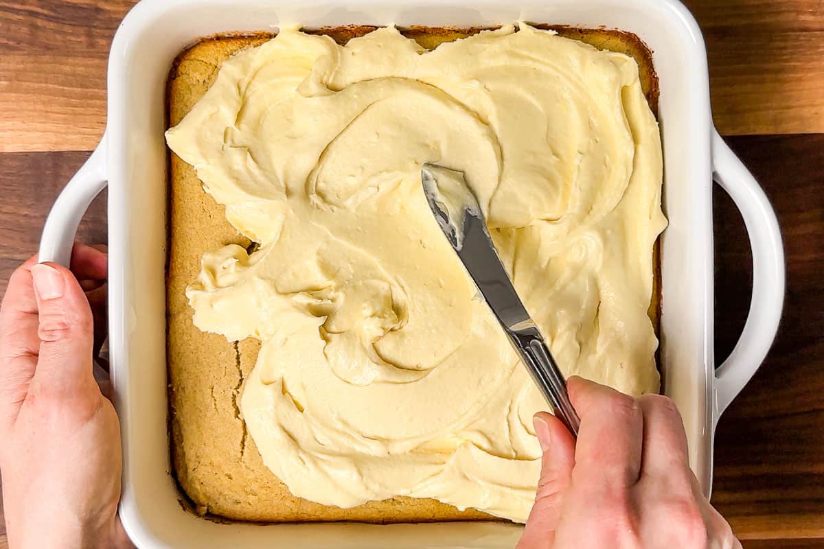 Spreading a cream cheese frosting over the top of the baked and cooled gluten free banana cake.