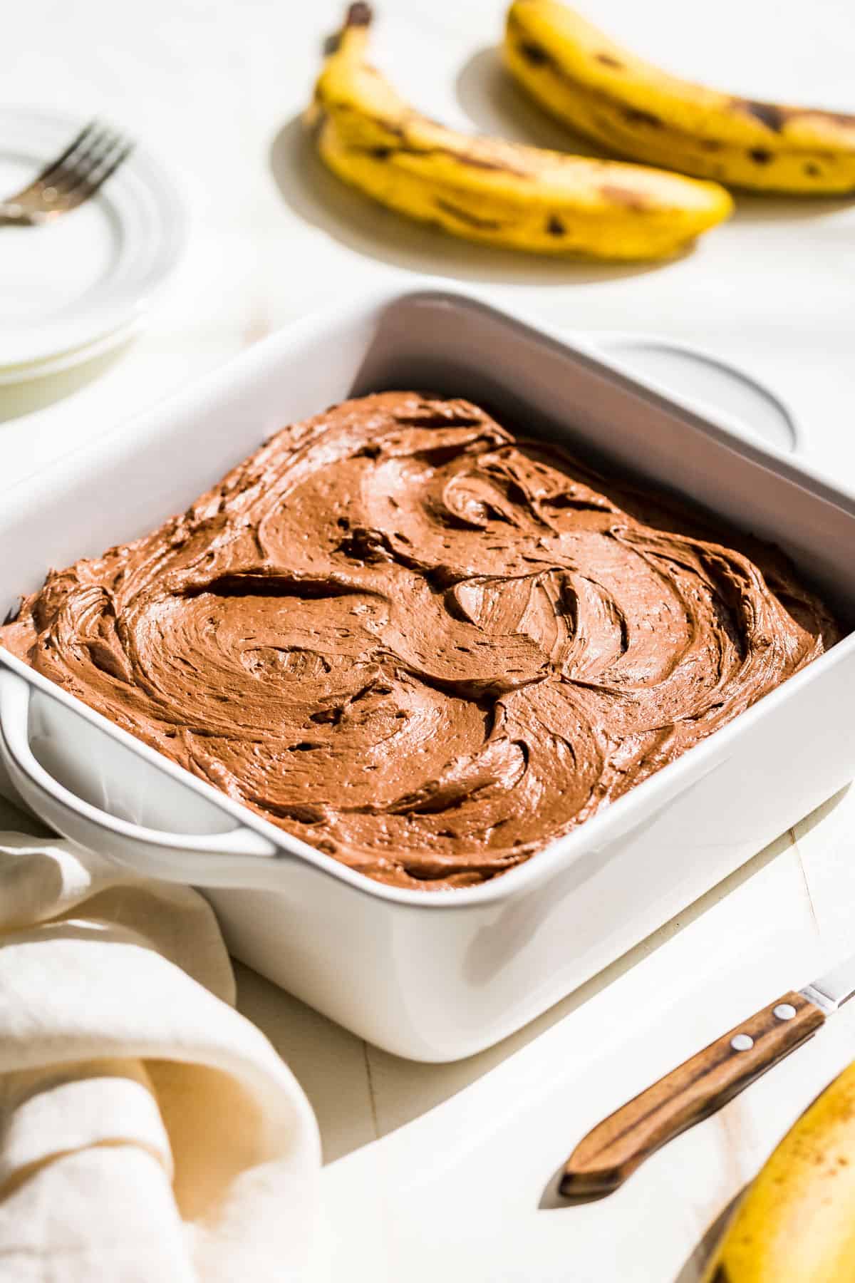 Gluten free banana cake in a white baking dish frosted with a chocolate buttercream.