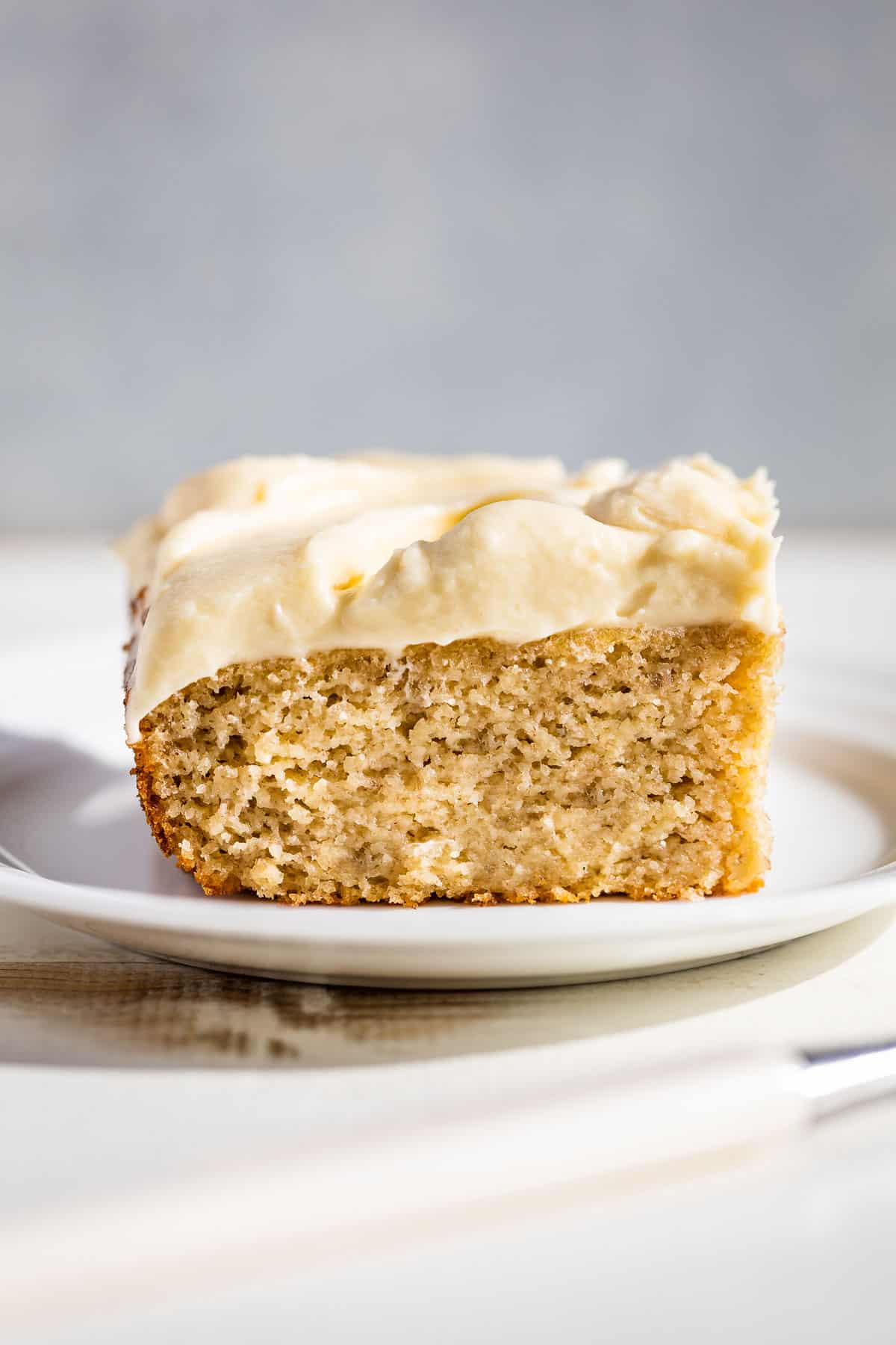 A slice of gluten free banana cake on a white plate with a blue background.