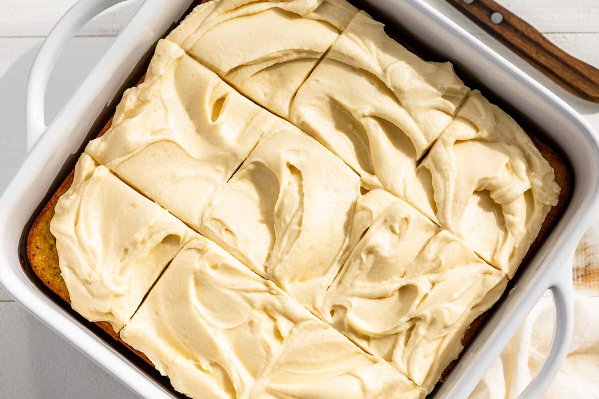 Straight down view gluten free banana cake frosted with cream cheese frosting and a wood knife on the side.