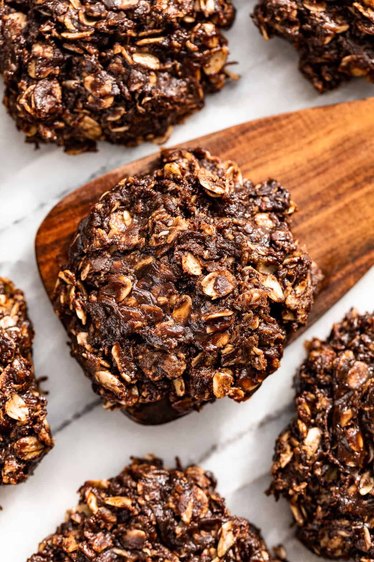 Healthy No Bake Cookies on a marble background with a wood spatula scooping one up.