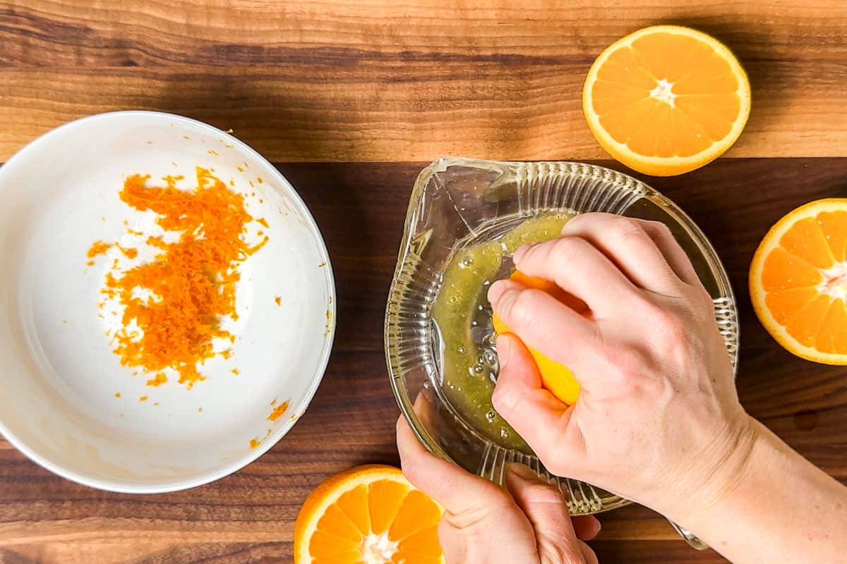 Zesting and juicing the oranges on a wood cutting board.