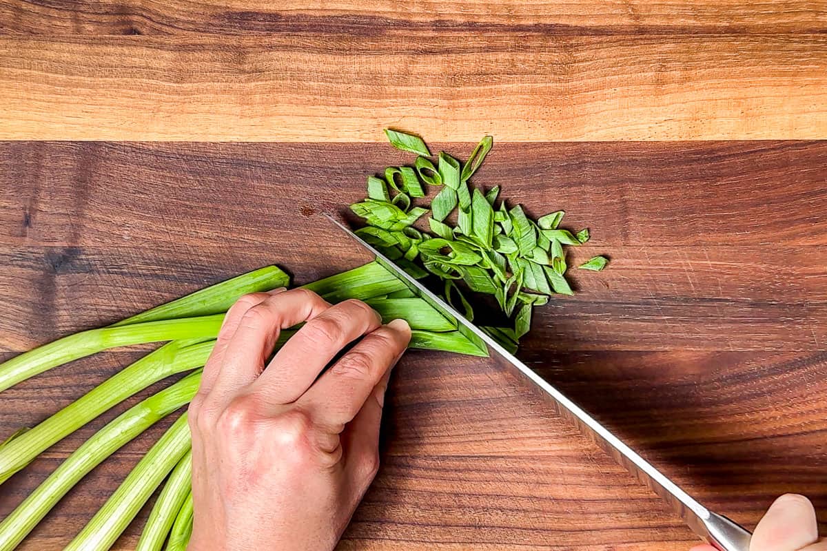 Slicing the green onions with a chef's knife on a wood cutting board.