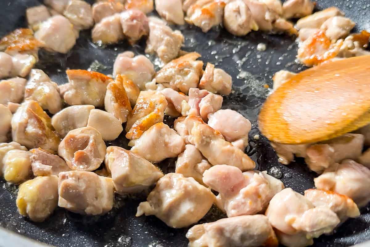 Sautéing the chicken in a skillet with a wooden spoon.