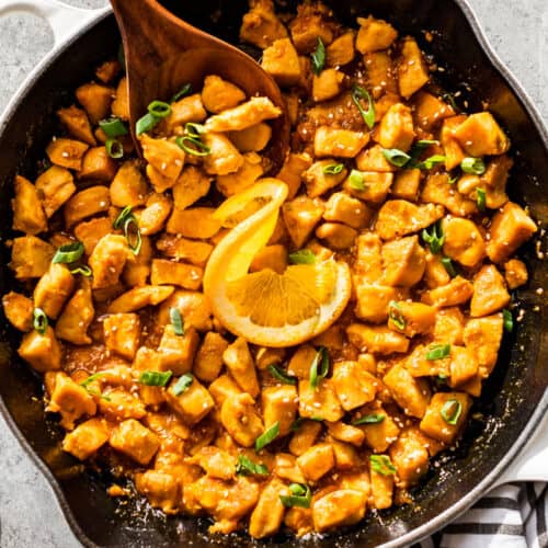 Straight down view of finished healthy orange chicken in a white enameled cast iron skillet.