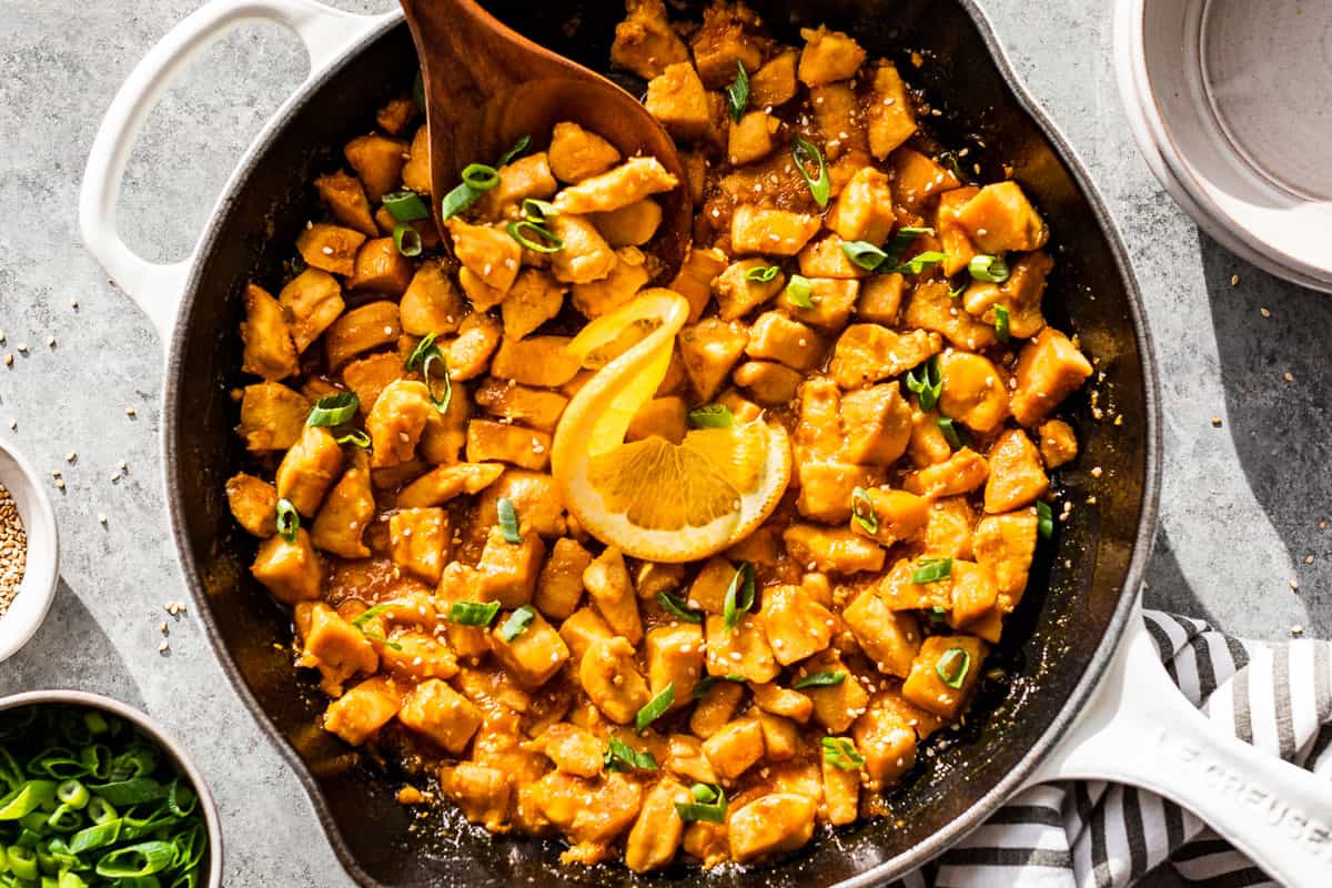 Straight down view of finished healthy orange chicken in a white enameled cast iron skillet.