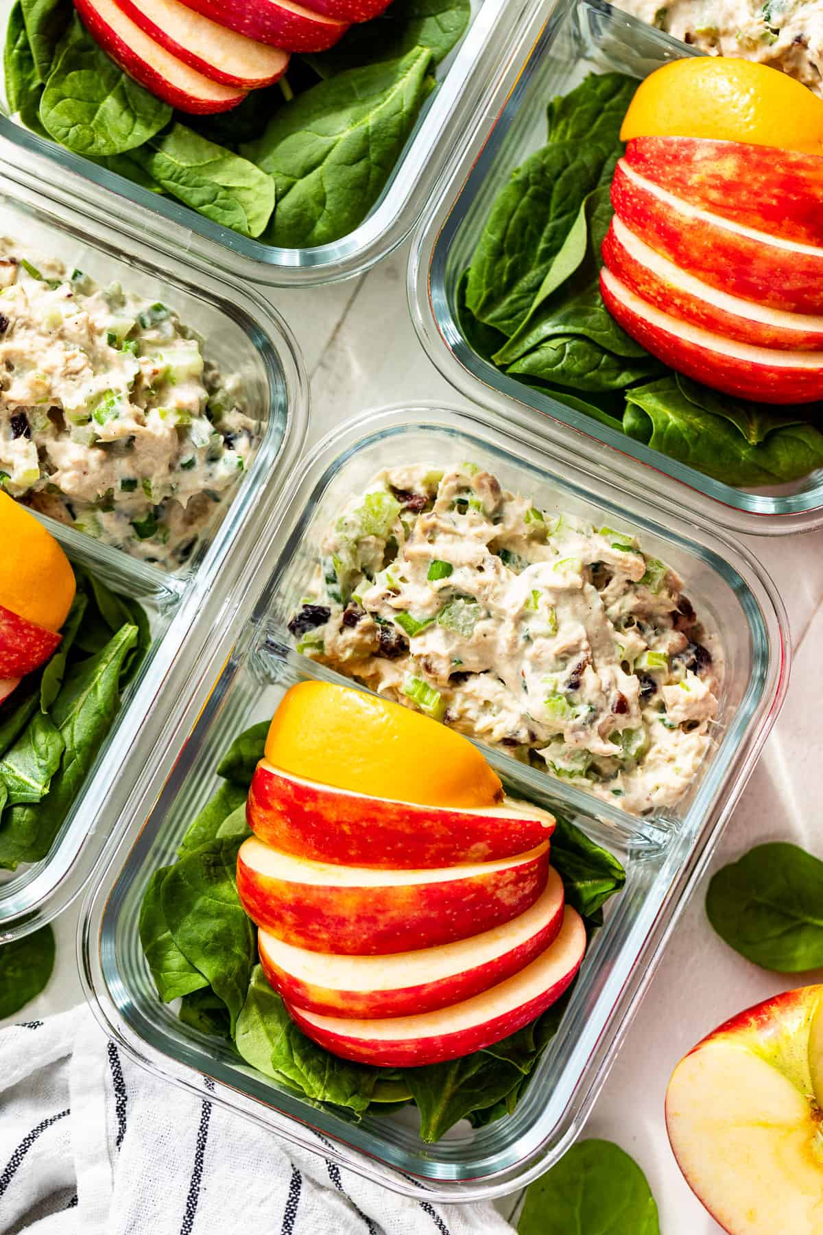 Straight down view of Healthy Tuna Salad in meal prep containers with spinach, sliced apples, and a lemon wedge on the side.