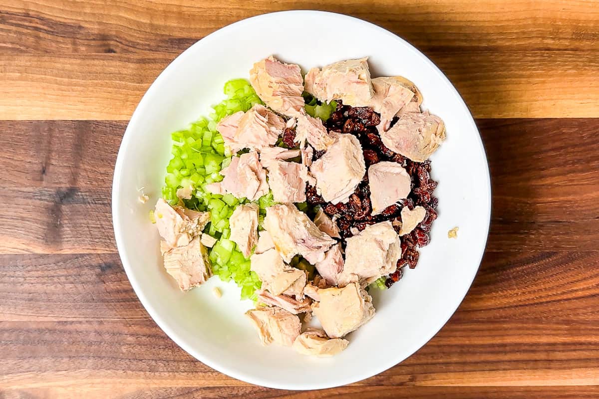 Canned tuna fish, celery, dried cranberries, and sliced green onion in a bowl.