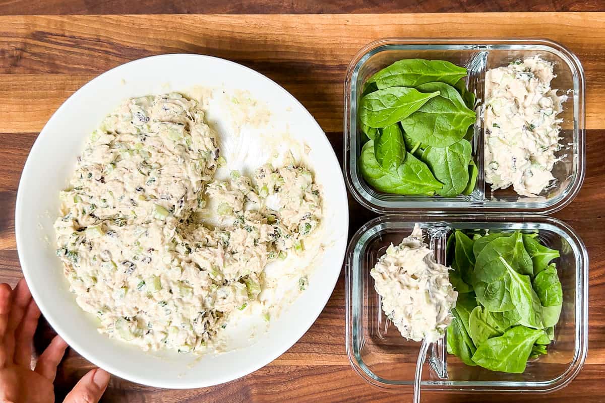 Spooning the finished Tuna Salad into meal prep containers with spinach on one side.