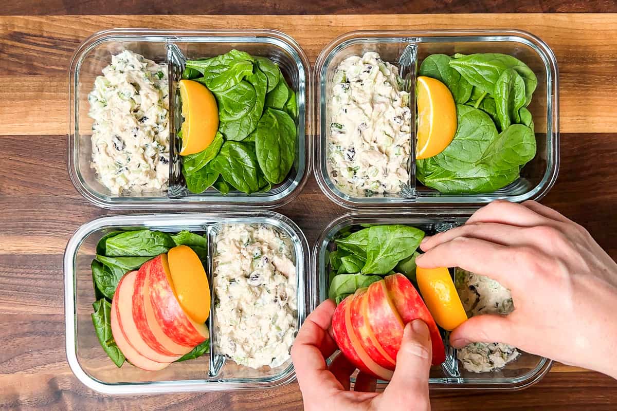 Adding sliced apple and lemon wedges to the Healthy Tuna Salad in meal prep containers.