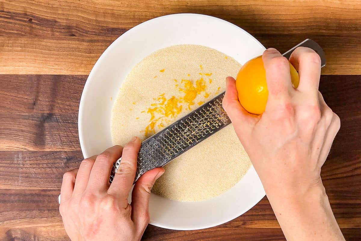 Zesting a lemon over a bowl of sugar on a wood cutting board.