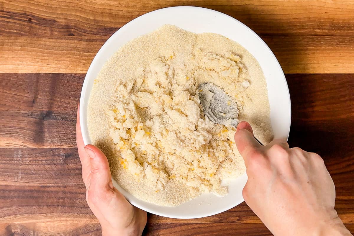 Mashing the coconut oil into the sugar and lemon zest on a wood cutting board.