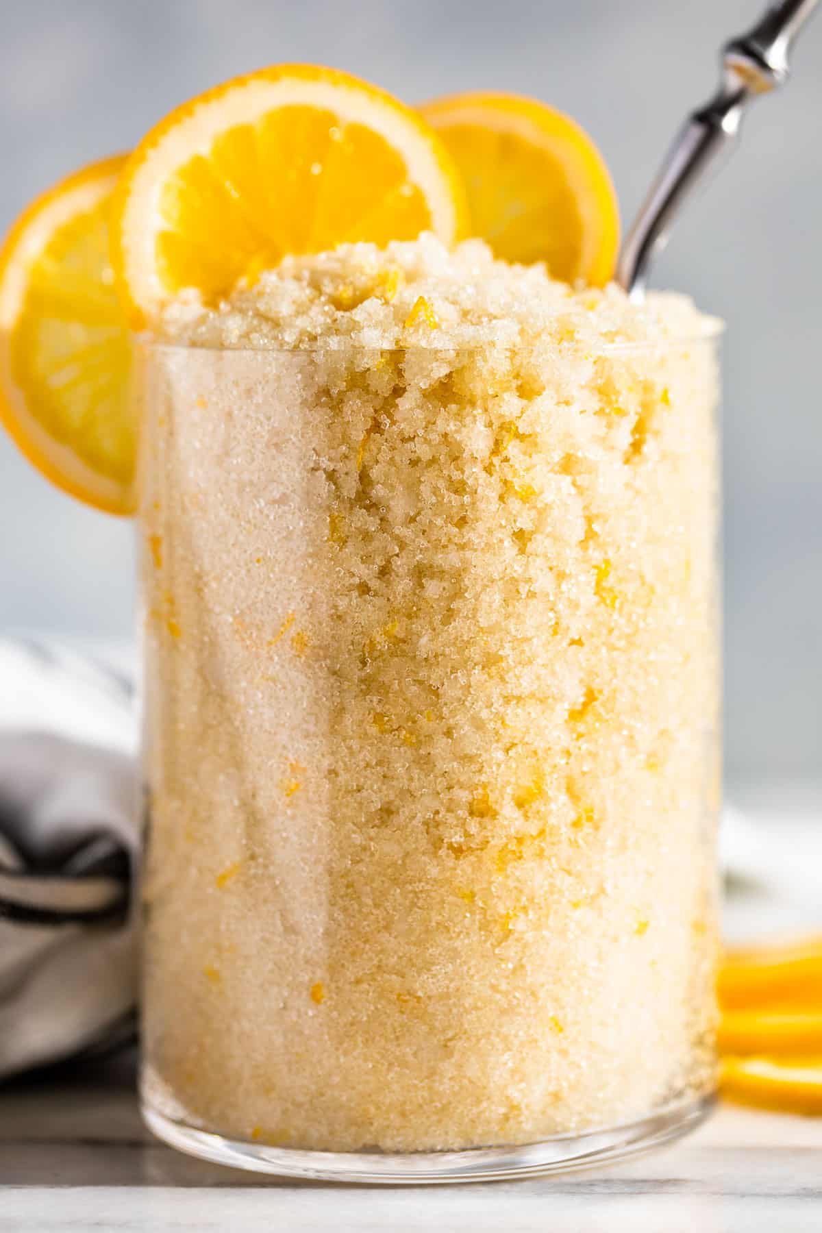 Close macro view of Lemon Sugar Scrub in a clear glass container with lemon slices on top.