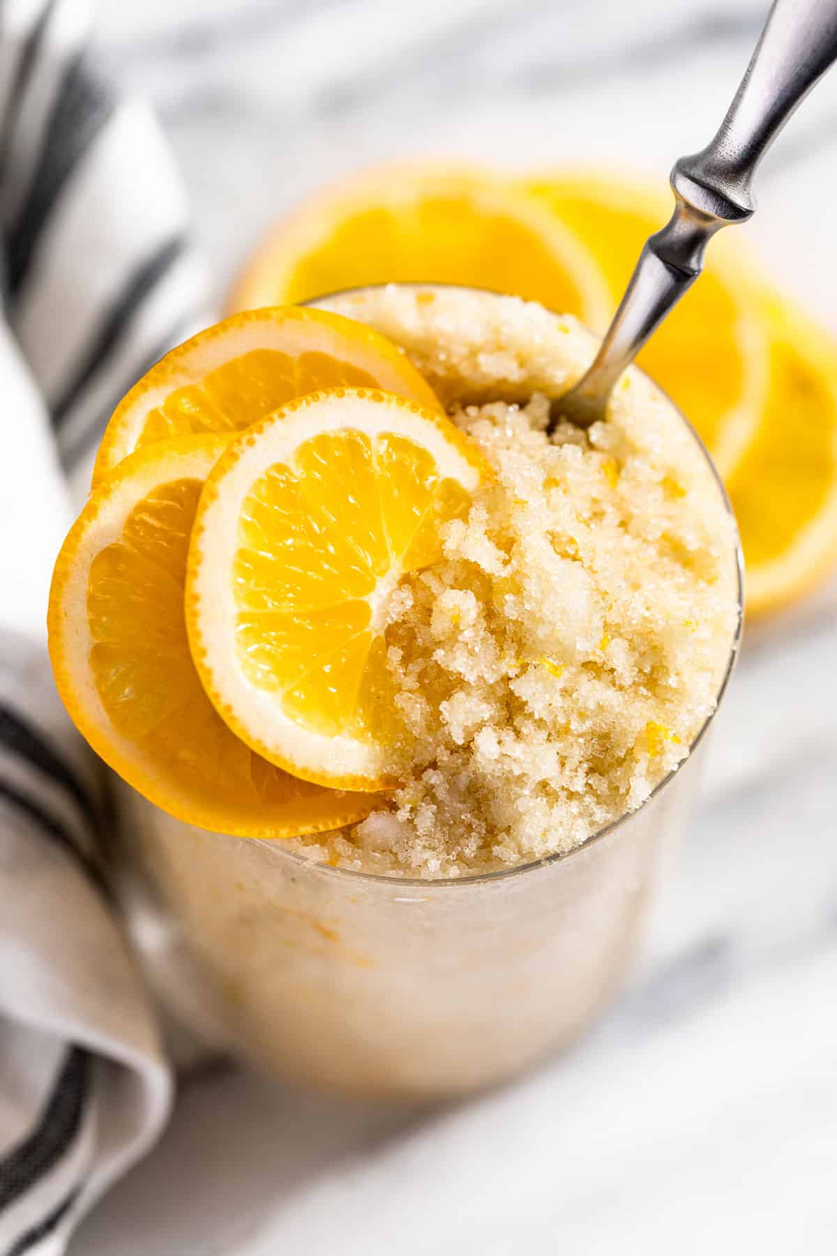 Looking down at Lemon Sugar Scrub in a clear glass container with lemon slices on top.