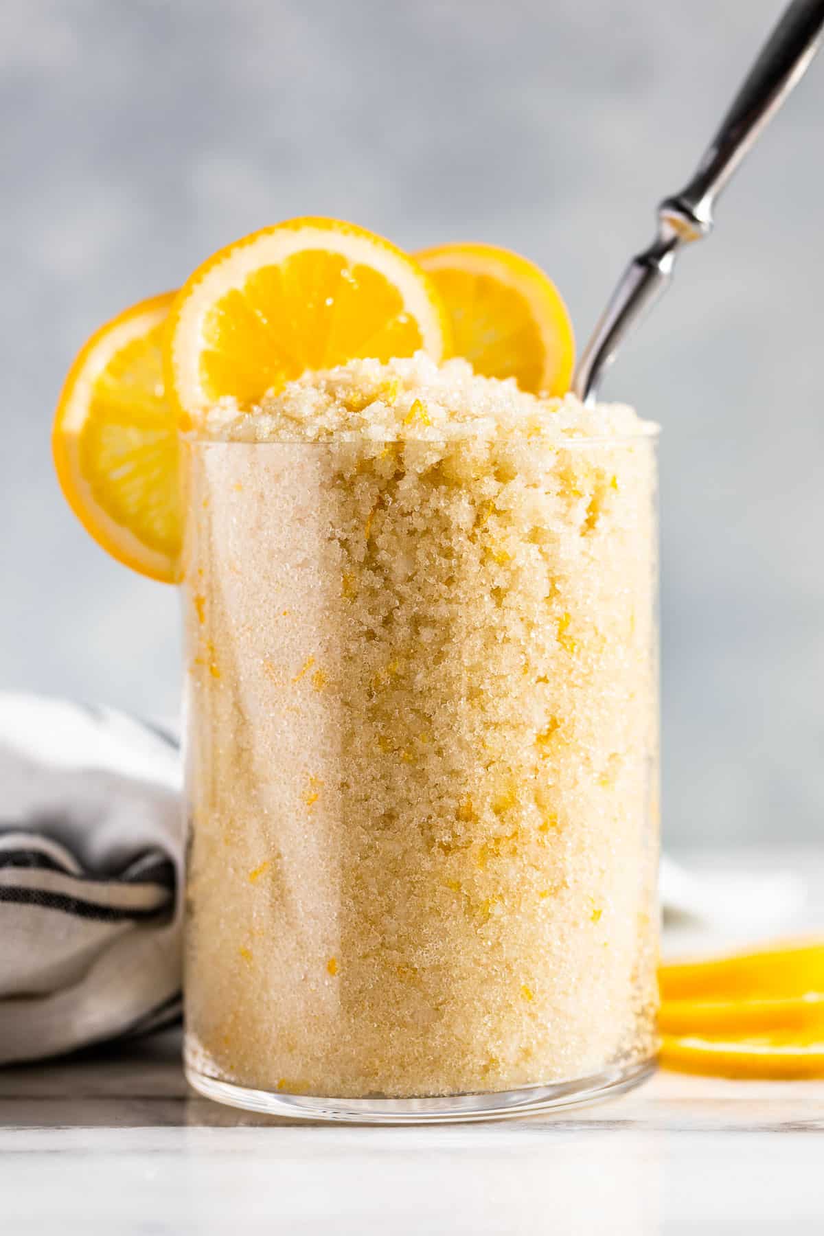 Lemon Sugar Scrub in a clear glass container with lemon slices on top.