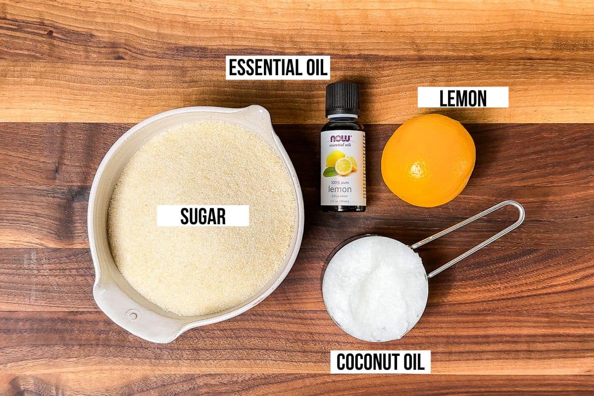 Sugar, coconut oil, a lemon, and lemon essential oil on a wood cutting board.