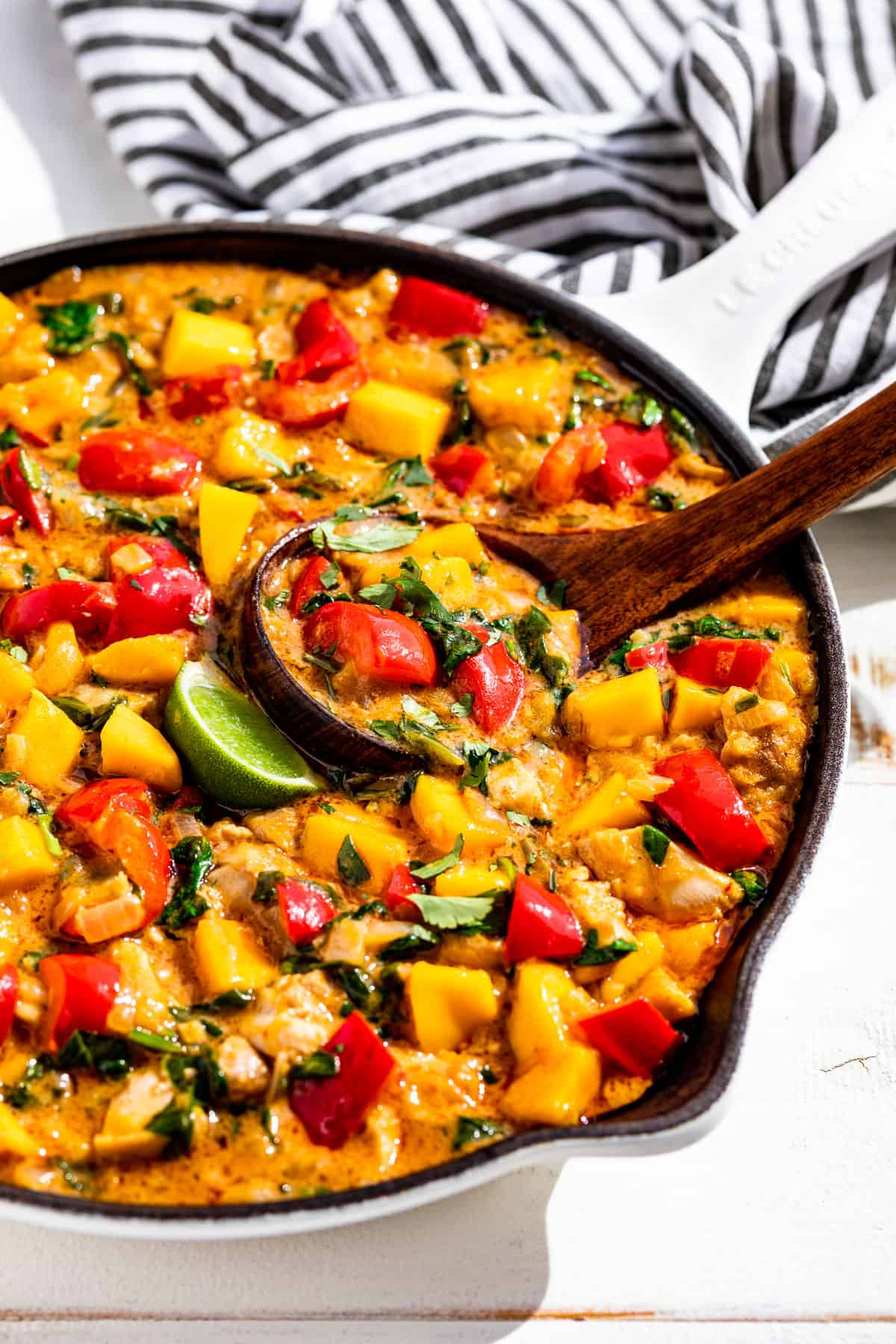 Side view of Mango Chicken Curry in a white skillet with a wood ladle scooping some out.